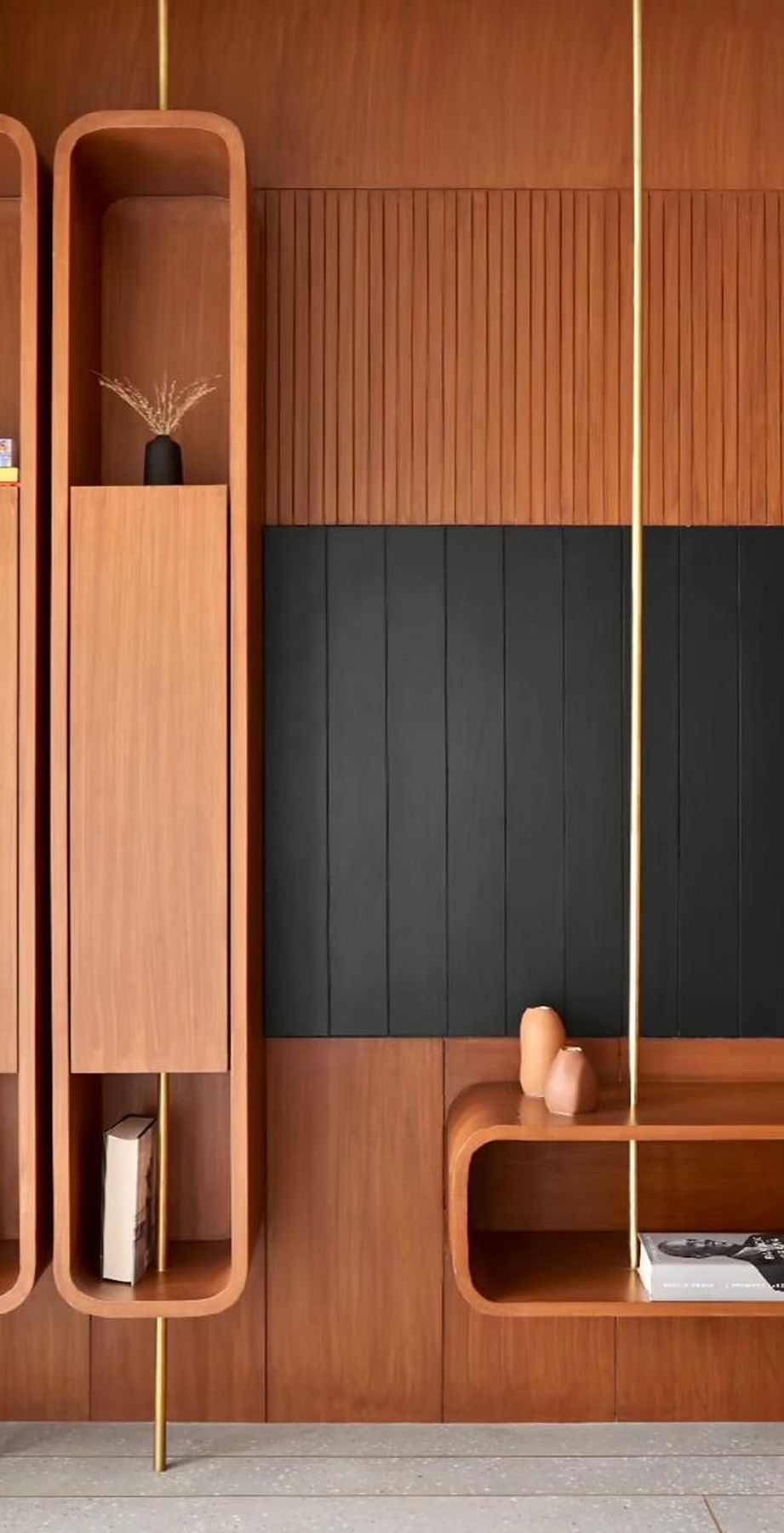 Teak joinery wall with rounded niches suspended on brass rods against a black fluted panel