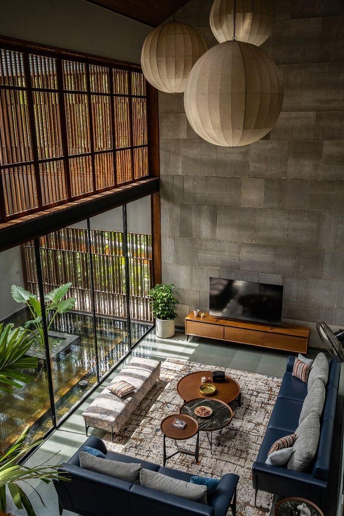 Double-height living room seen from above, with paper lanterns, a stone-clad wall and a timber screen
