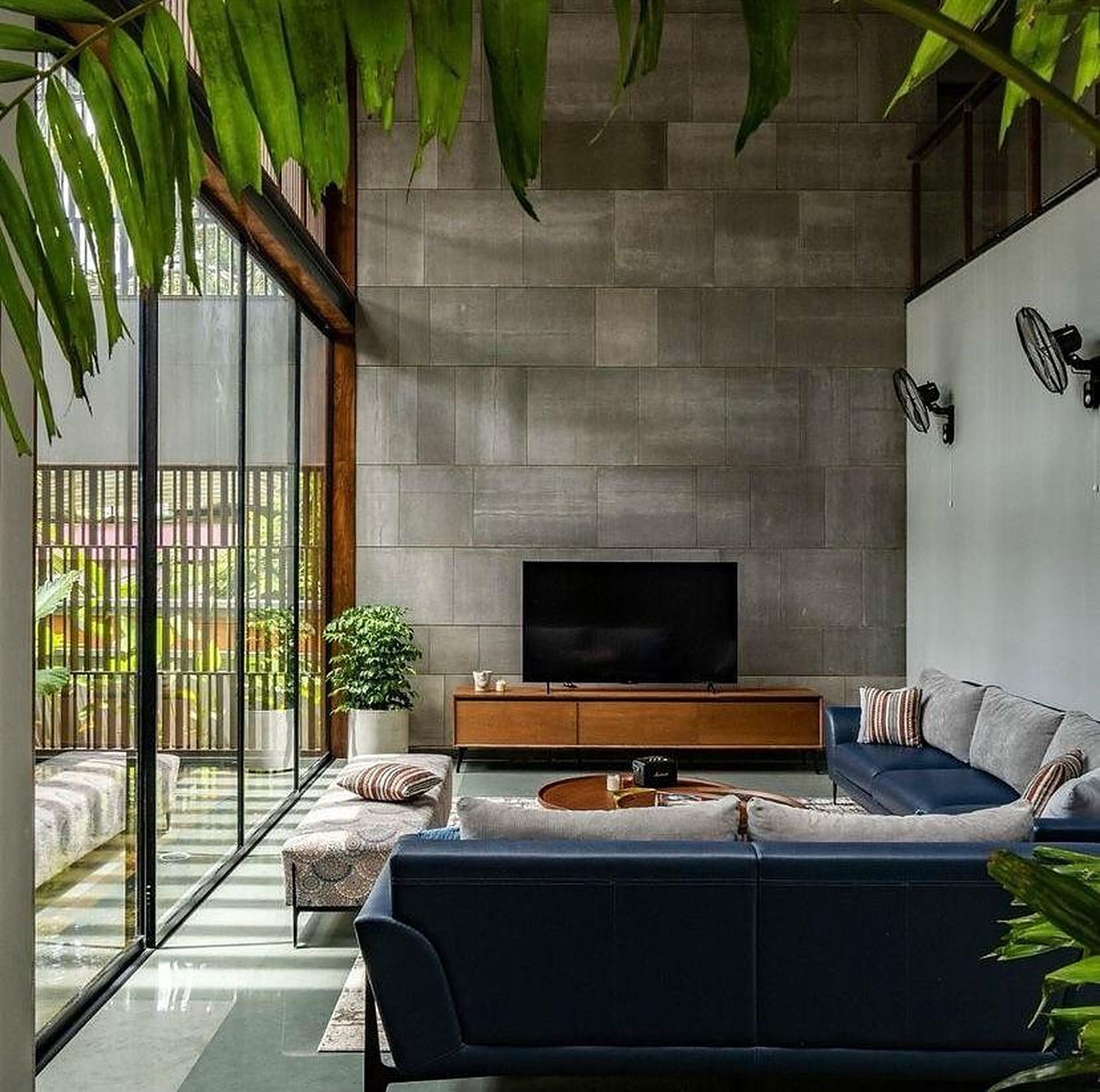 Living room with navy sofas, a grey stone wall and a glass wall onto a planted court